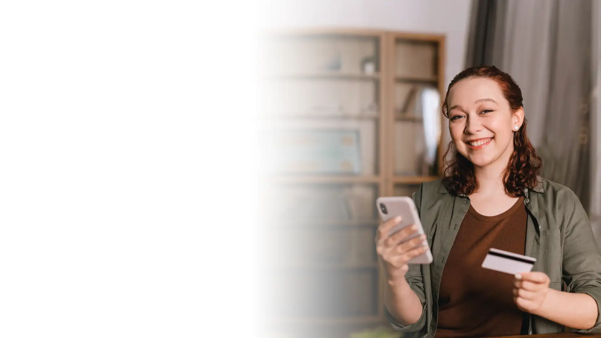chica jóven sonriendo con un celular en una mano y una tarjeta de crédito en la otra simulando un pago online